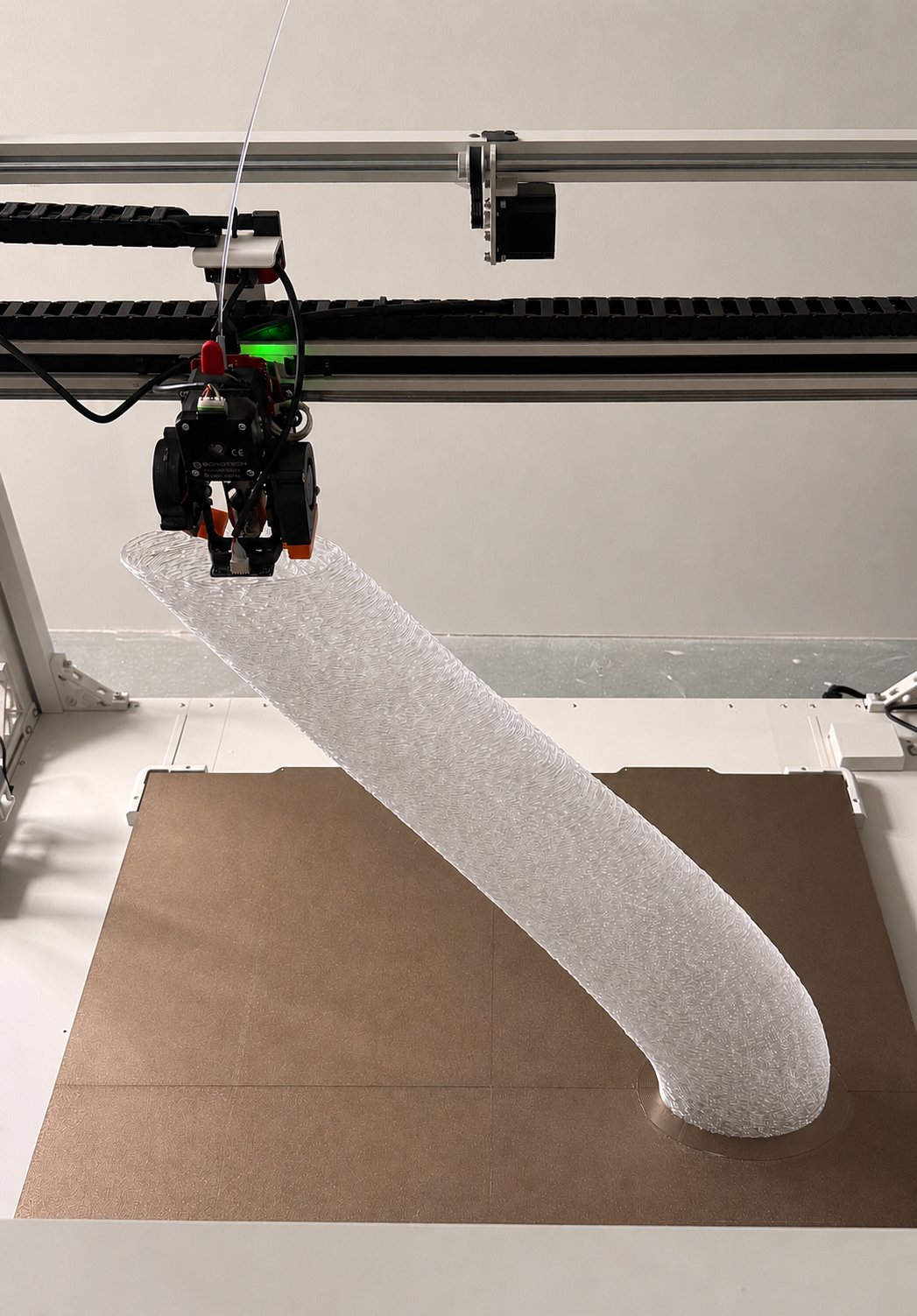 Large-format 3D printer mid-print, extruding a tall translucent sculptural part